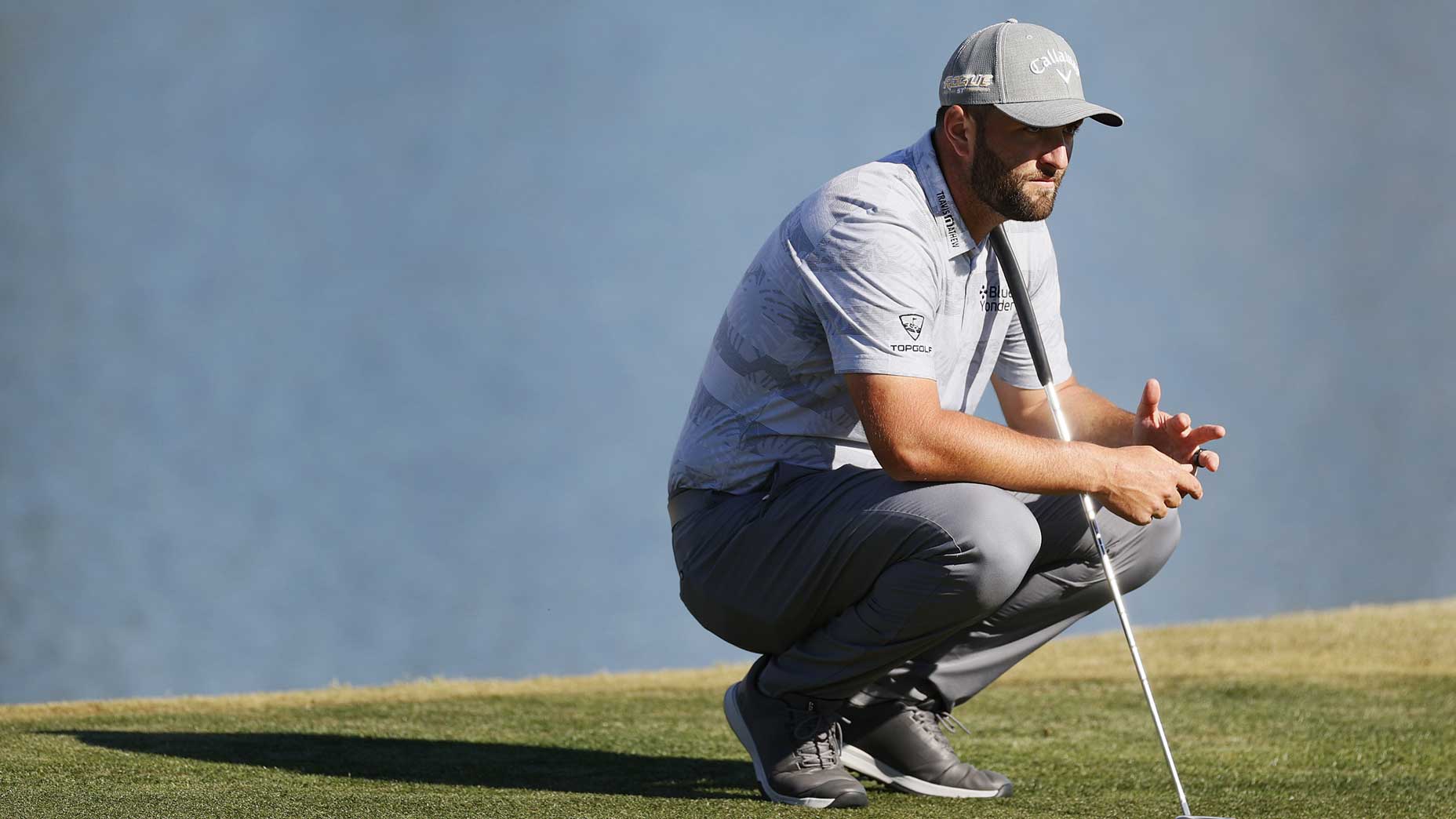 Jon Rahm crouches on putting green