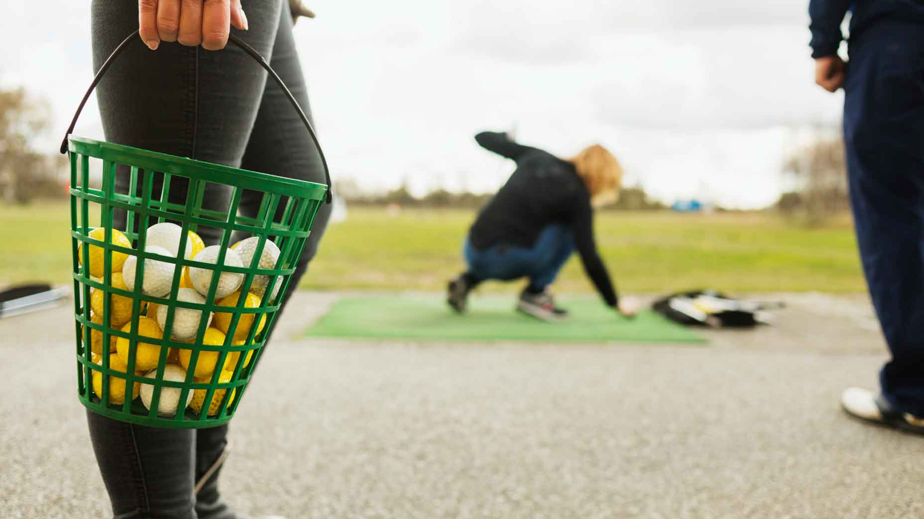 woman holding bucket of balls at driving range