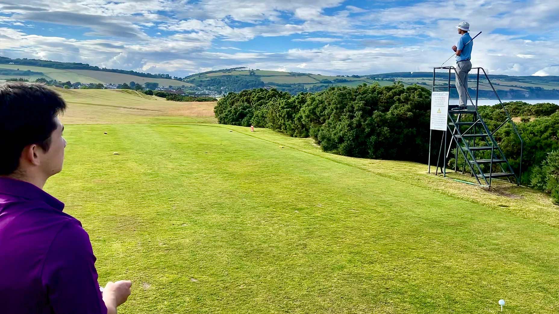 Two golfers look at on a hole, one from a small observation platform off the tee.