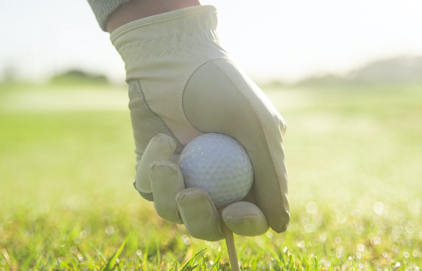 Hand wearing a golf glove putting a golf ball on a tee