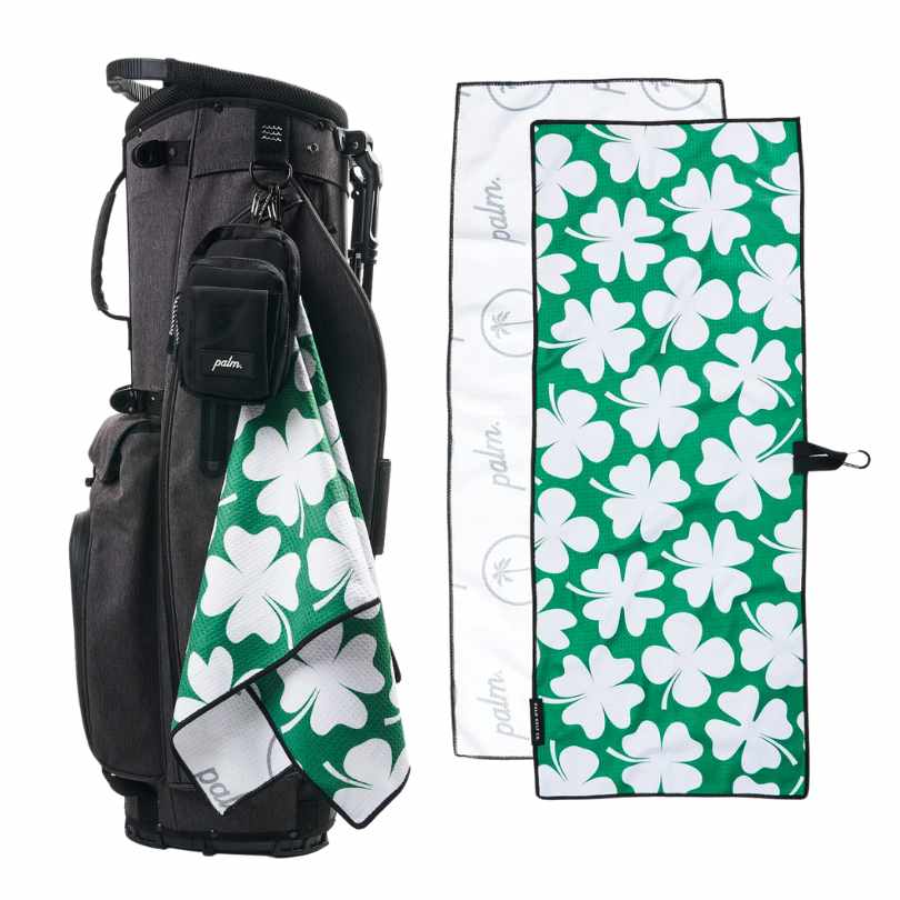 PALM GOLF CO. GET LUCKY TOWEL - golf towel with green background and white 4-leaf clovers large repeat pattern. Towel as a snap CARABINER clip to hook onto your golf bag. Back of towel is white.