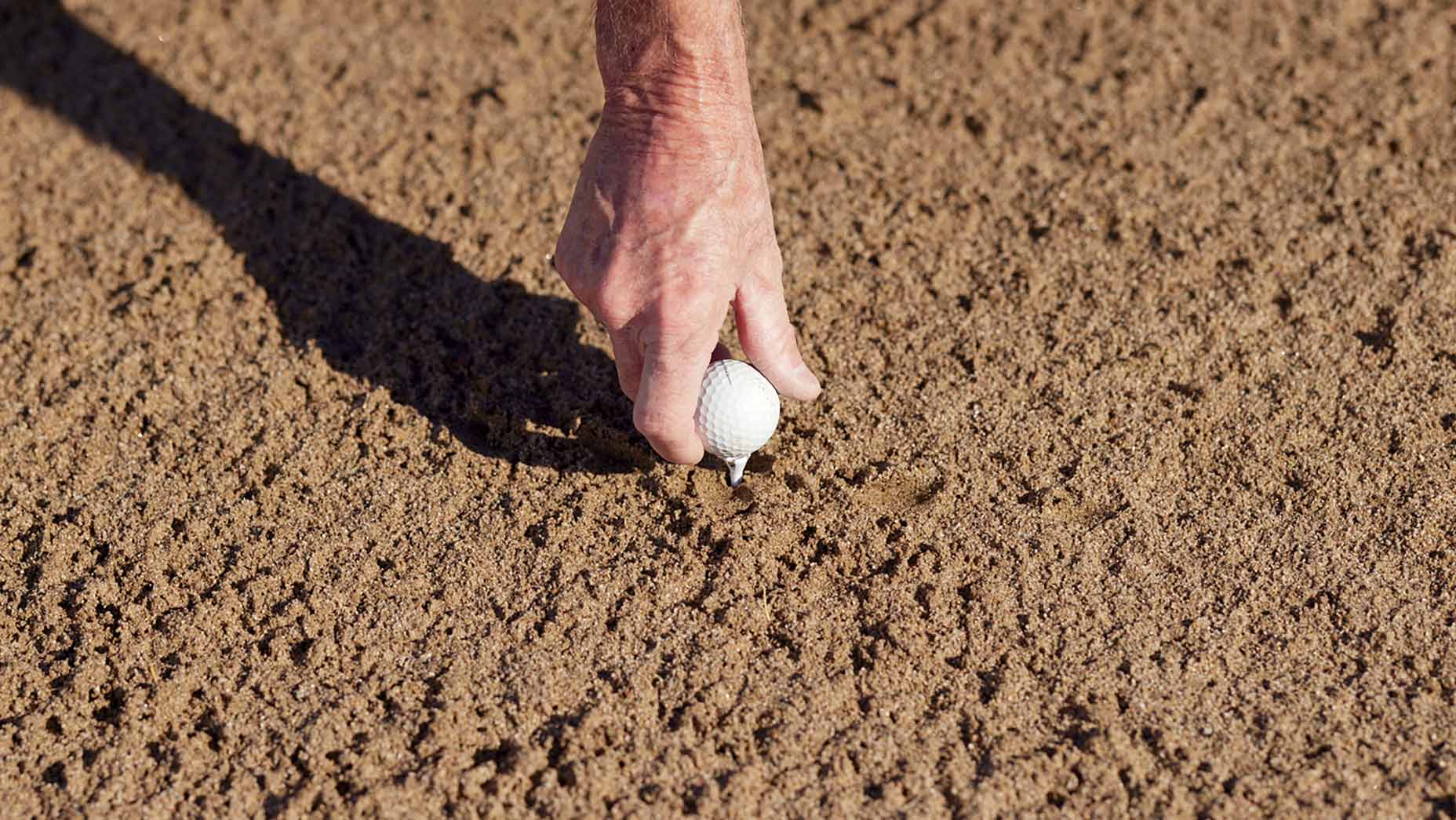 hand tees up ball in the sand