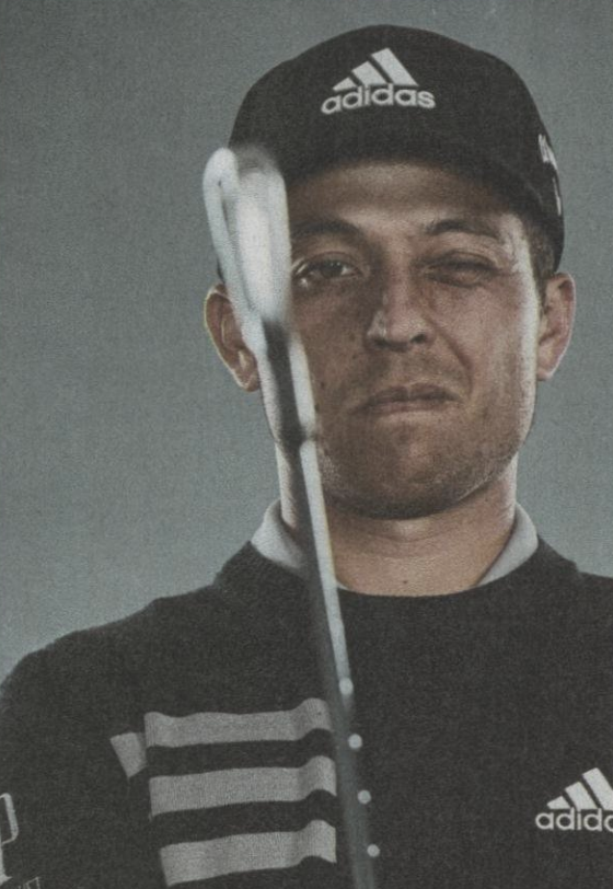 xander schauffele closes one eye and looks down club shaft toward the camera
