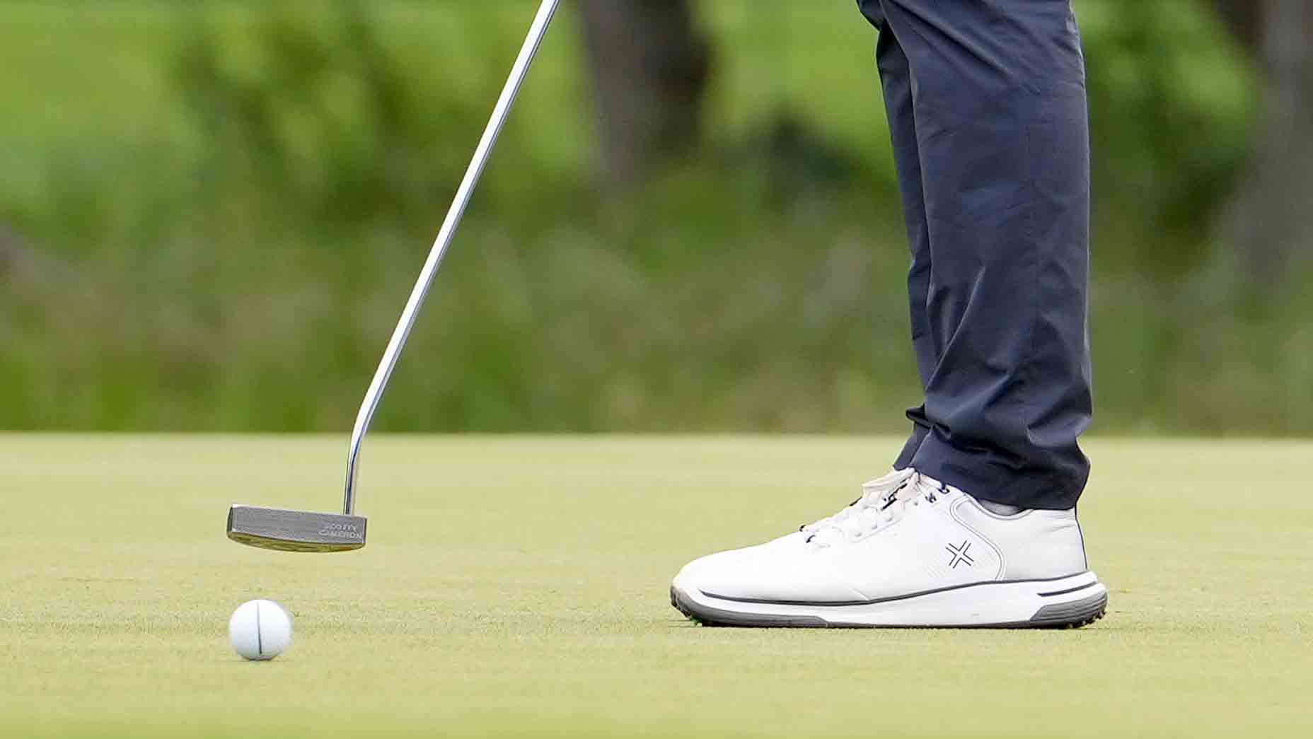 golfer in white shoes and blue pants hits putt