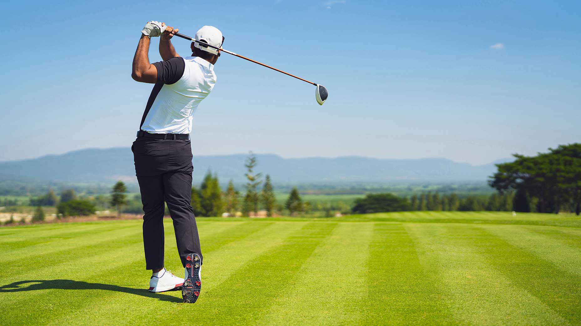 golfer swings on golf course with mountains in background