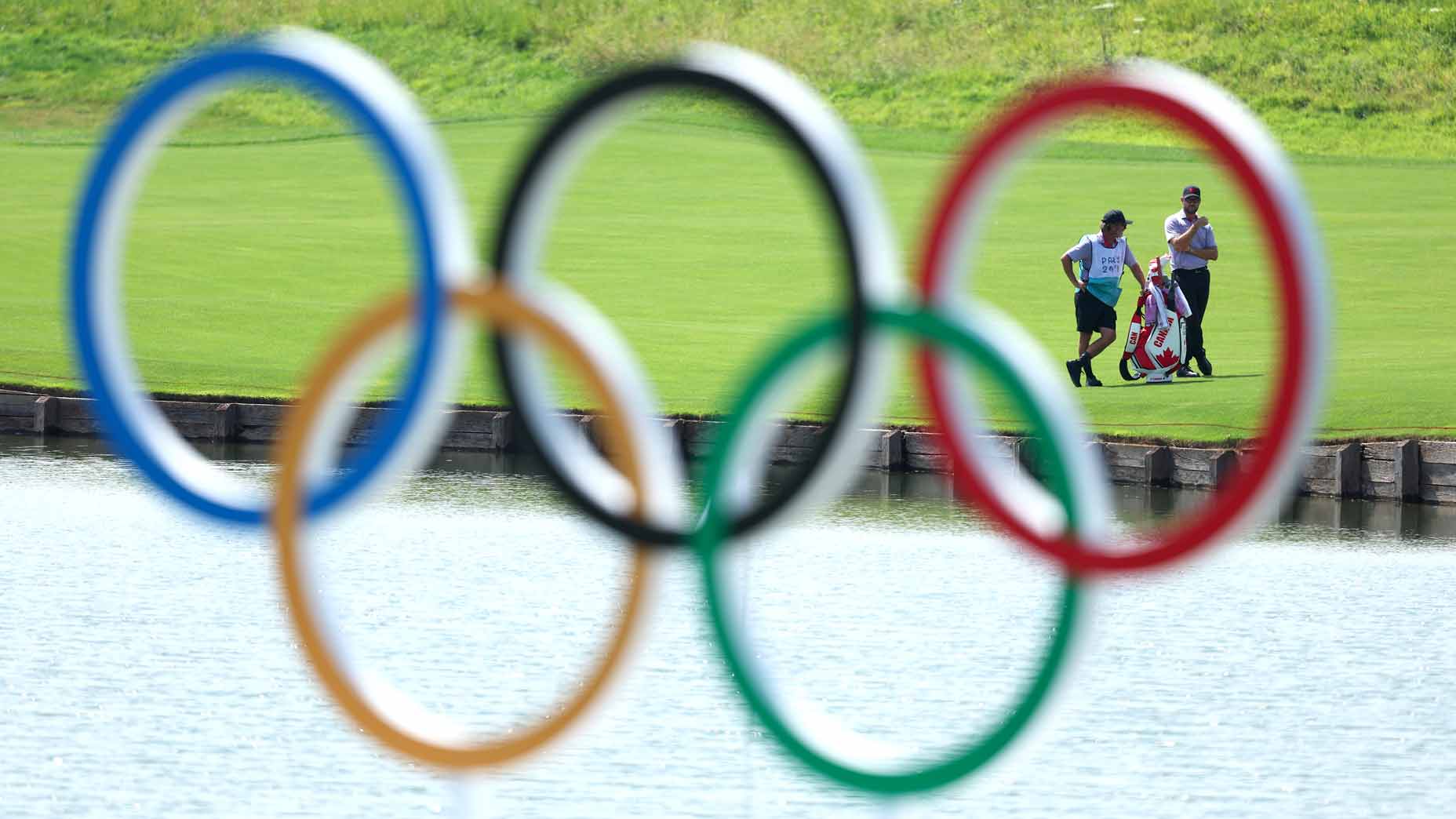 Corey Conners interacts with his caddie on the 15th hole with a view of the Olympic rings at the 2024 Olympics in Paris.