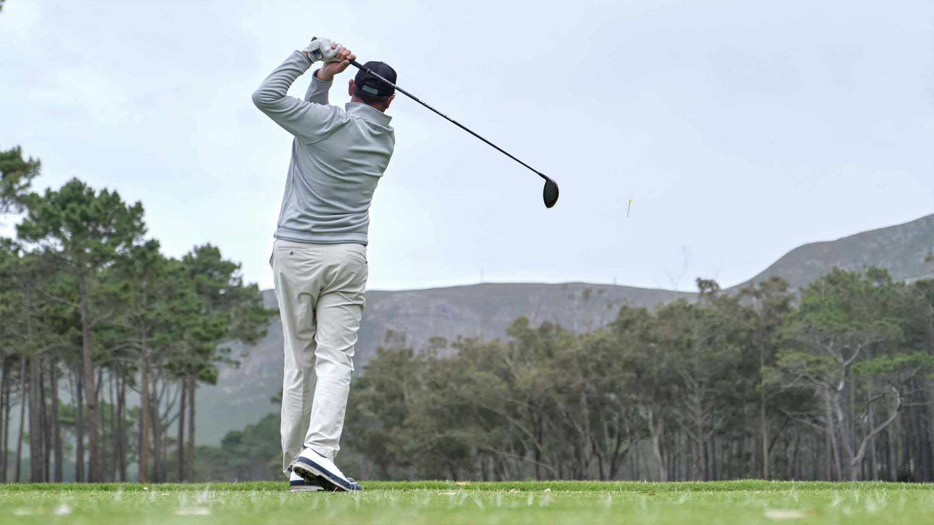 A golfer hits a driver on a golf course.