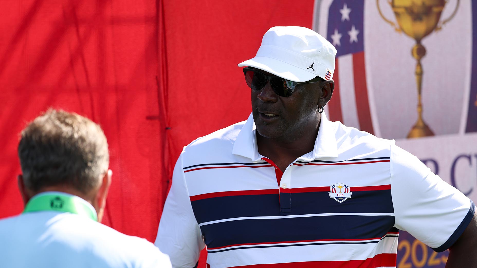 Michael Jordan smiles at the Ryder Cup at Bethpage Black in a U.S. team shirt and hat.