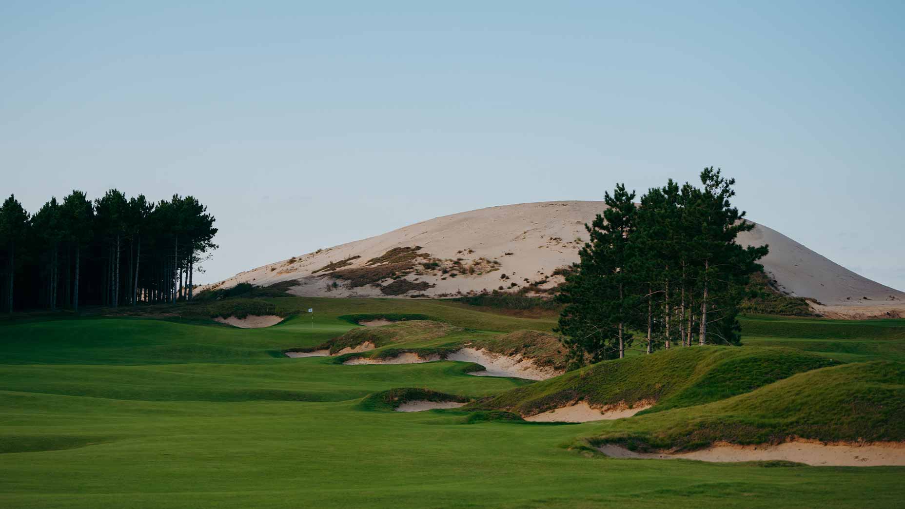 A shot of the first hole at the commons at sand valley with a large mound of sand in the background